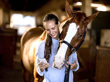 Junge Frau hält ihr Pferd am Halfter und liest eine Handynachricht 554x416-Weiterempfehlung-Frau-handy-gutesHalfter.png